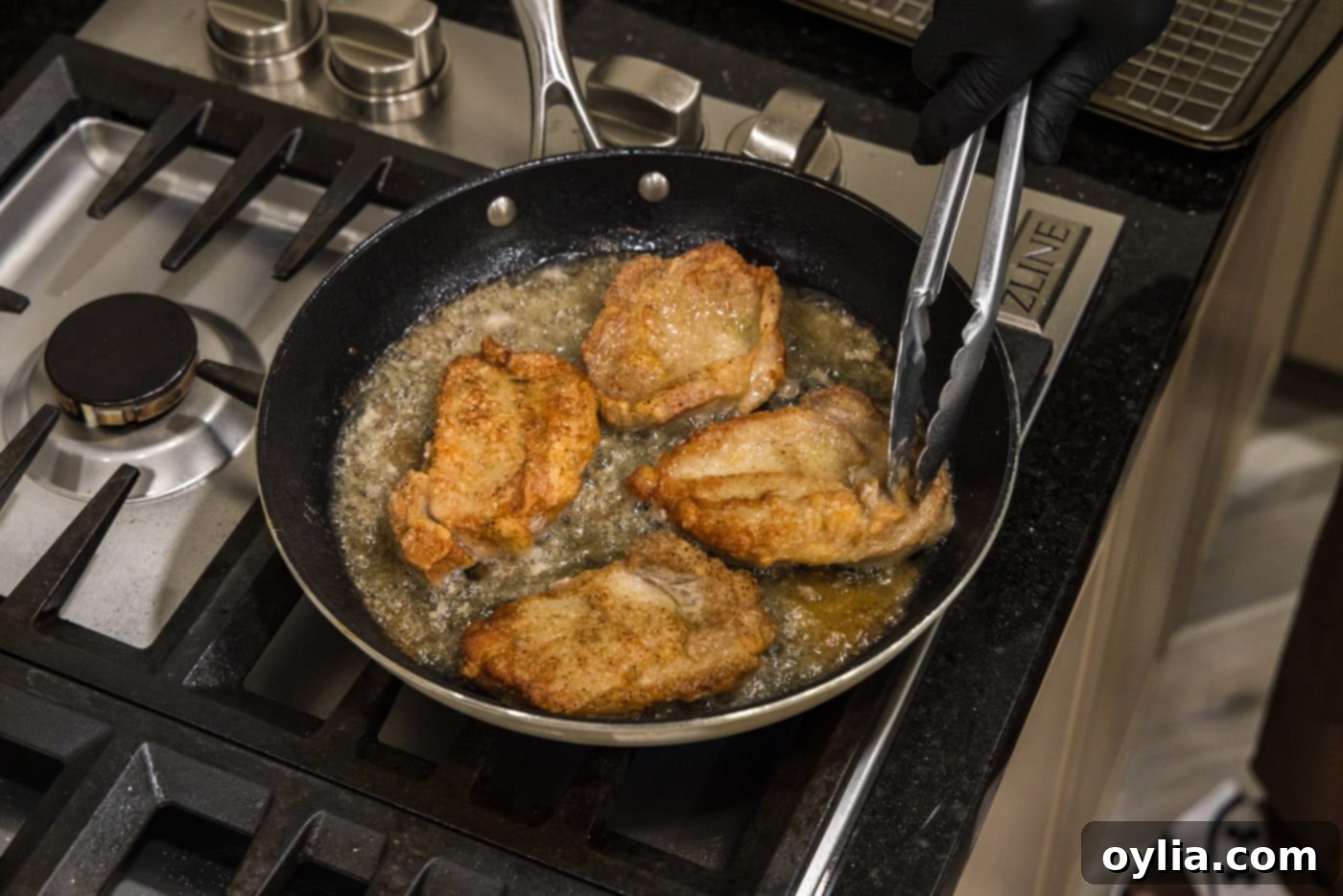 Tongs flipping veal chops in a skillet to cook evenly.