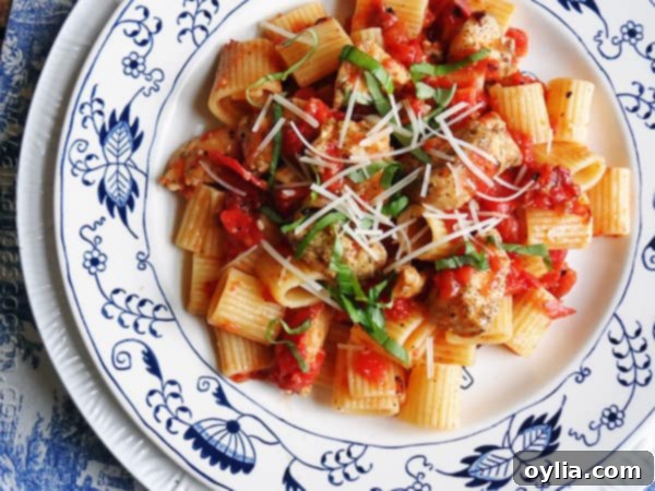 An overhead of a plate of spiced chicken and mezzi rigatoni topped with grated Parmigiano-Reggiano cheese and fresh basil.