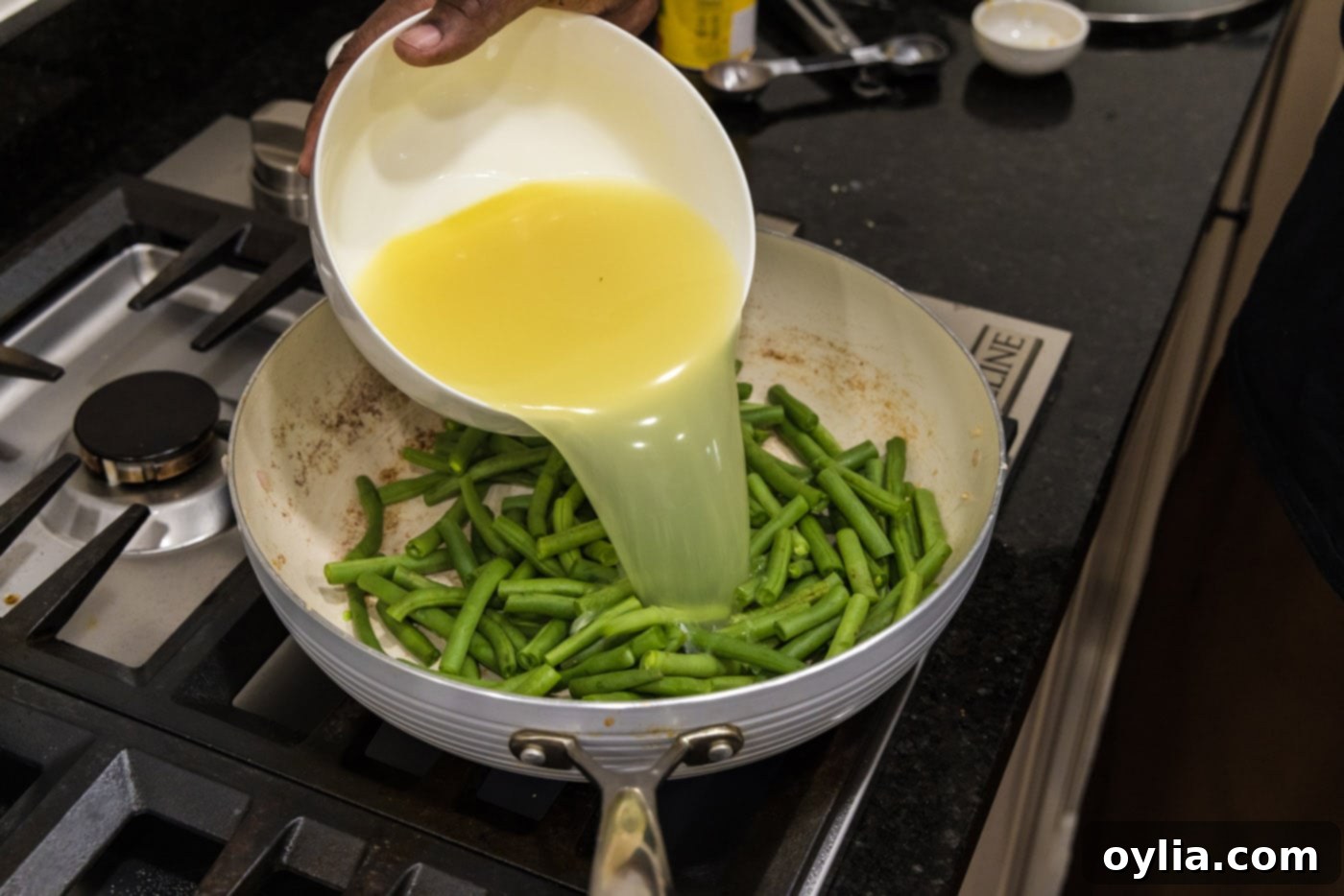 Pouring chicken stock into a skillet containing fresh green beans