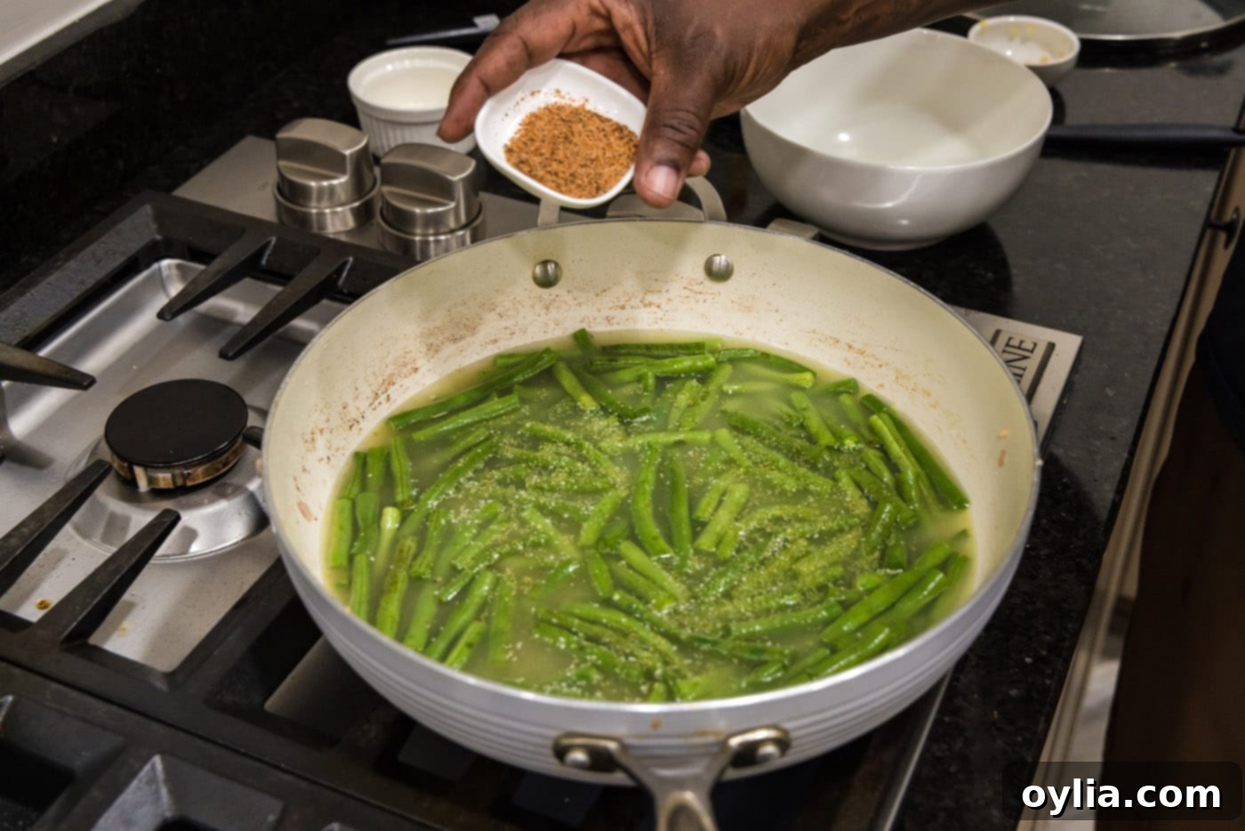 Adding Cajun seasoning to green beans simmering in a skillet