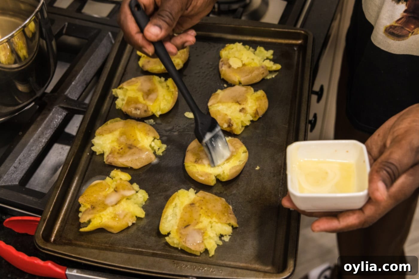 rubbing smashed potatoes with melted butter on a baking sheet