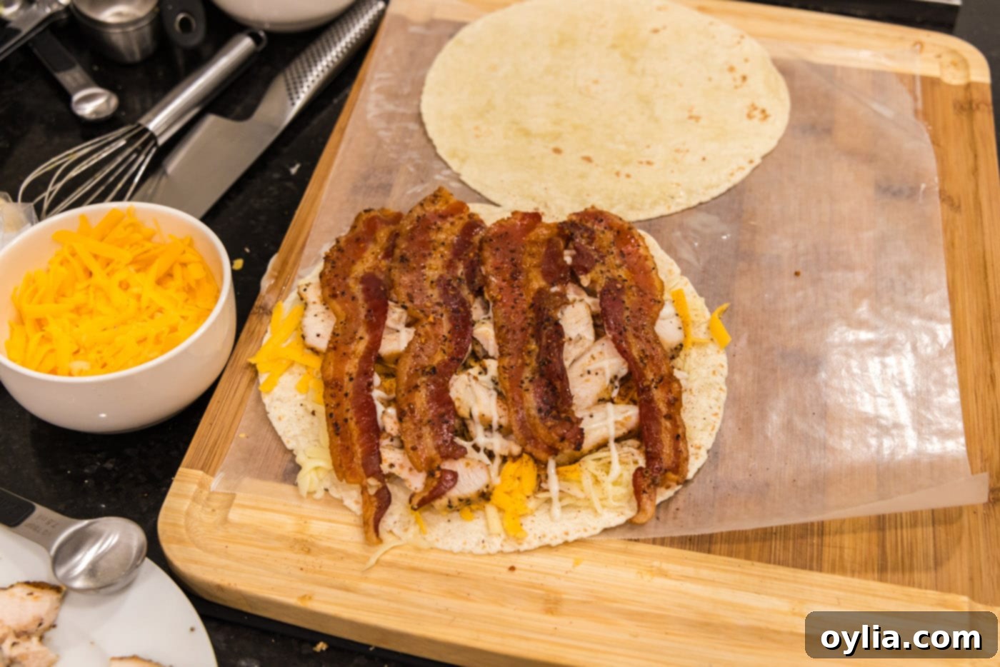 Sliced bacon layered over ranch, chicken, and cheese on a tortilla