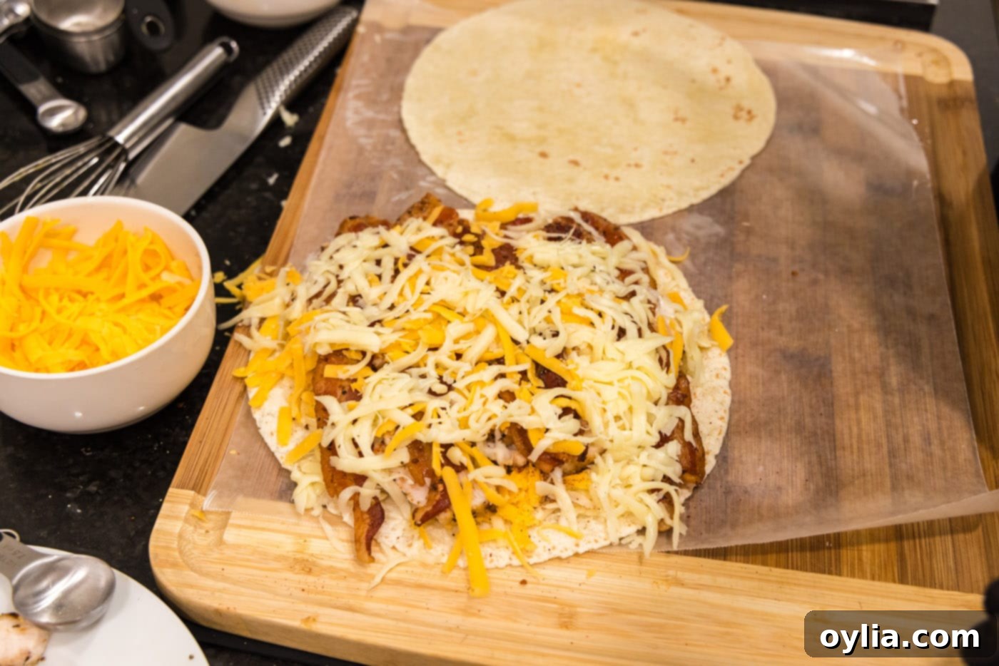 Shredded cheese over the top of bacon, ranch, and chicken on a tortilla