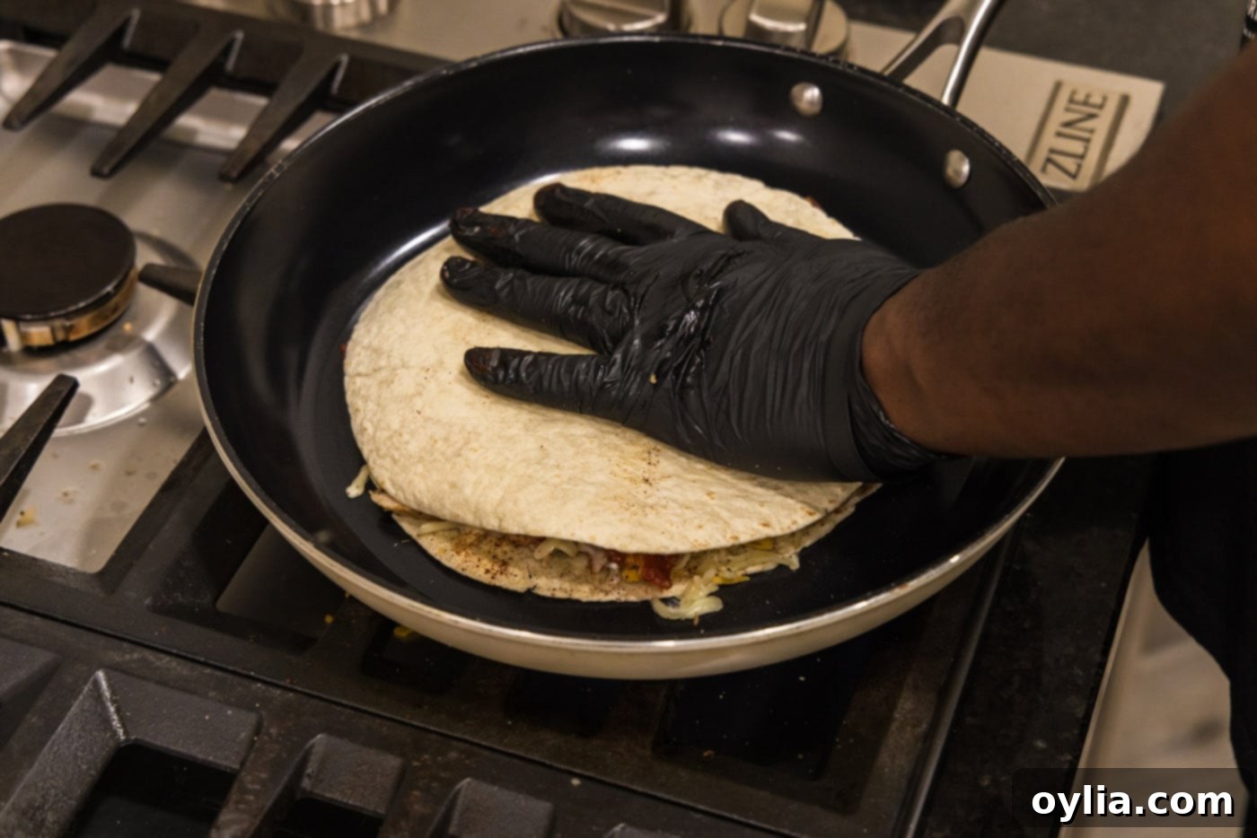 Hand pressing down tortilla shell over the top of quesadilla in a skillet