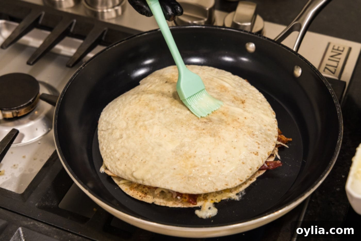 Basting tortilla shell with melted butter in a skillet, preparing for the flip