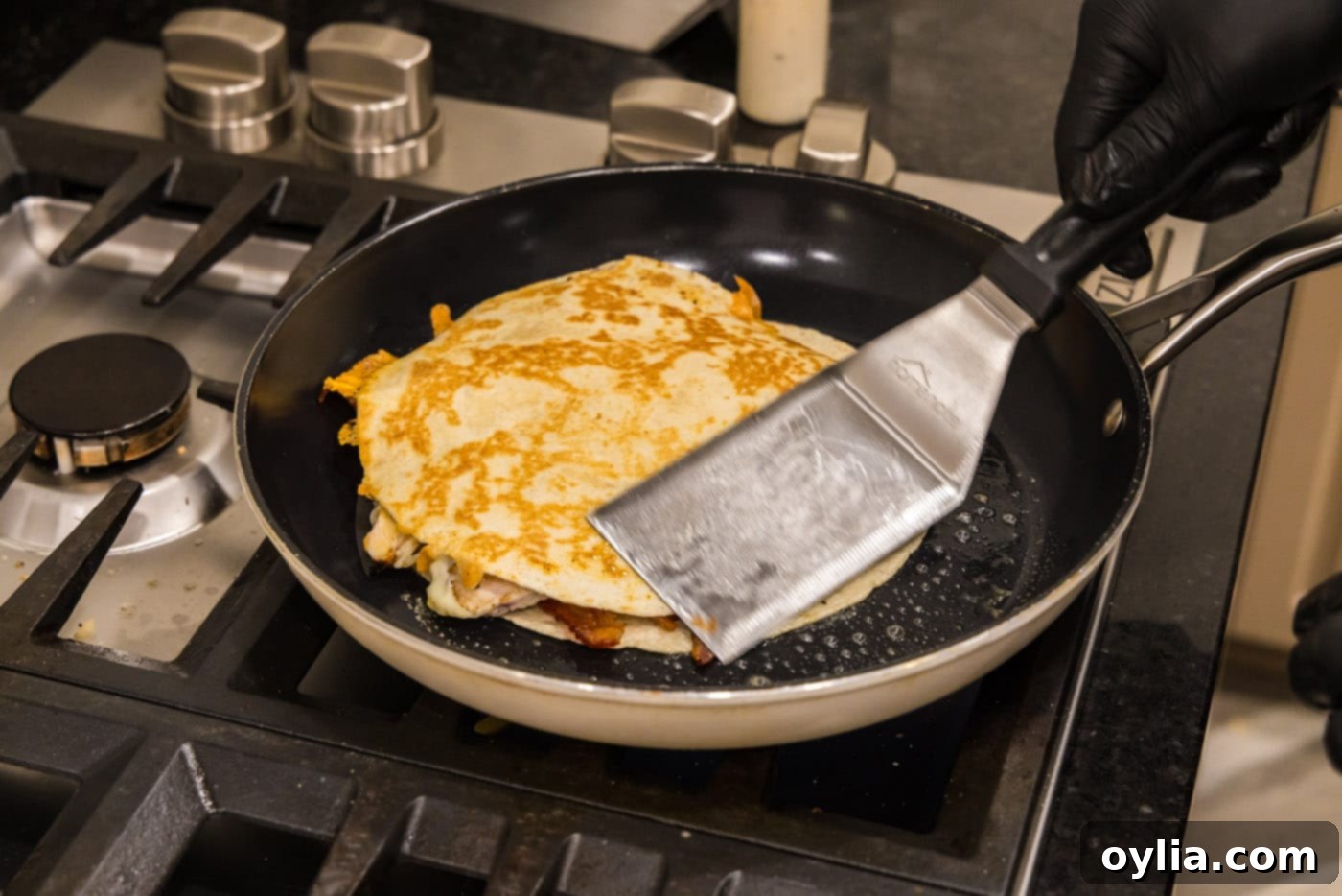 Fish turner spatula flipping a chicken bacon ranch quesadilla in a skillet