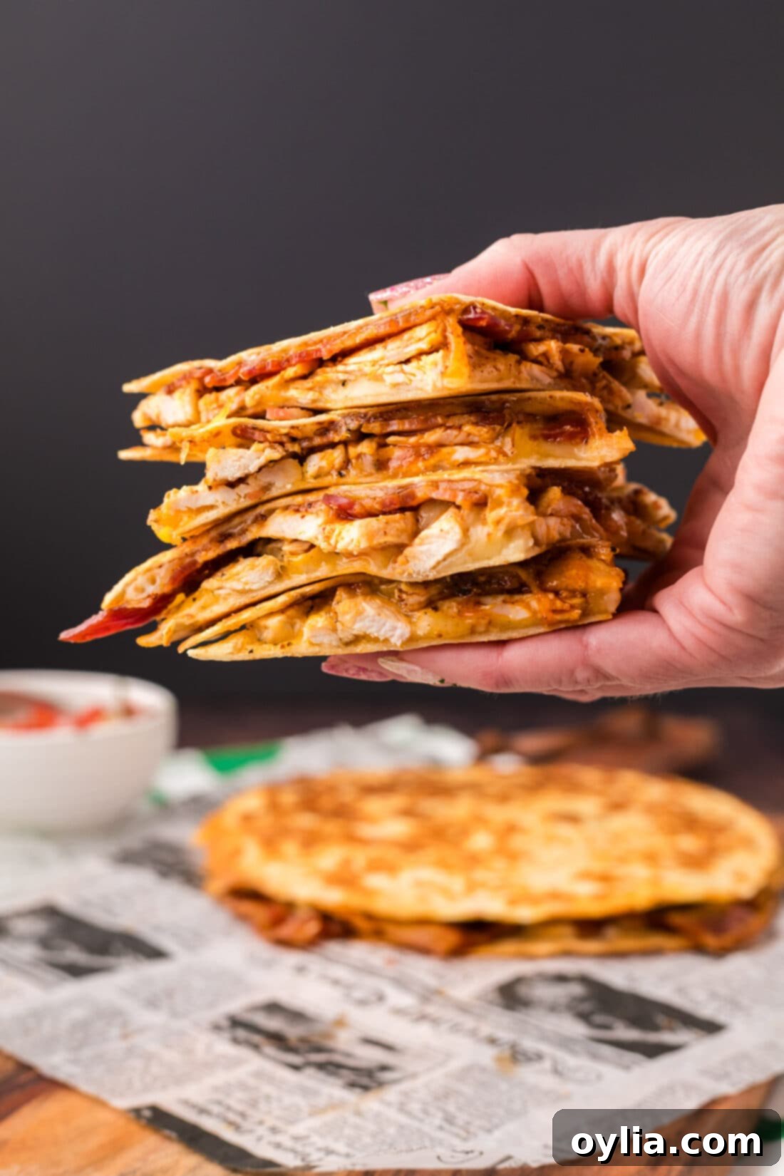 Hand holding up a stack of Chicken Bacon Ranch Quesadillas, showcasing the delicious filling and crispy tortilla.