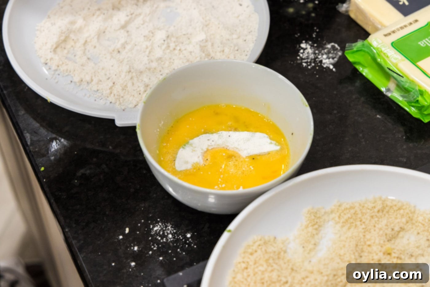 A floured avocado slice being dipped into a bowl of whisked egg