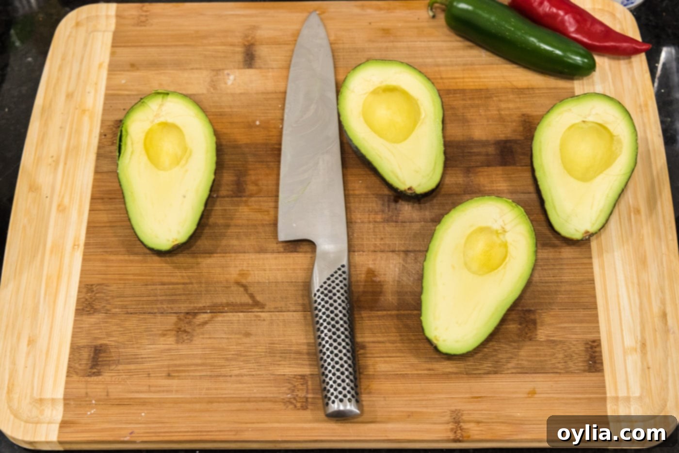 A knife resting on a cutting board next to several perfectly sliced avocado halves