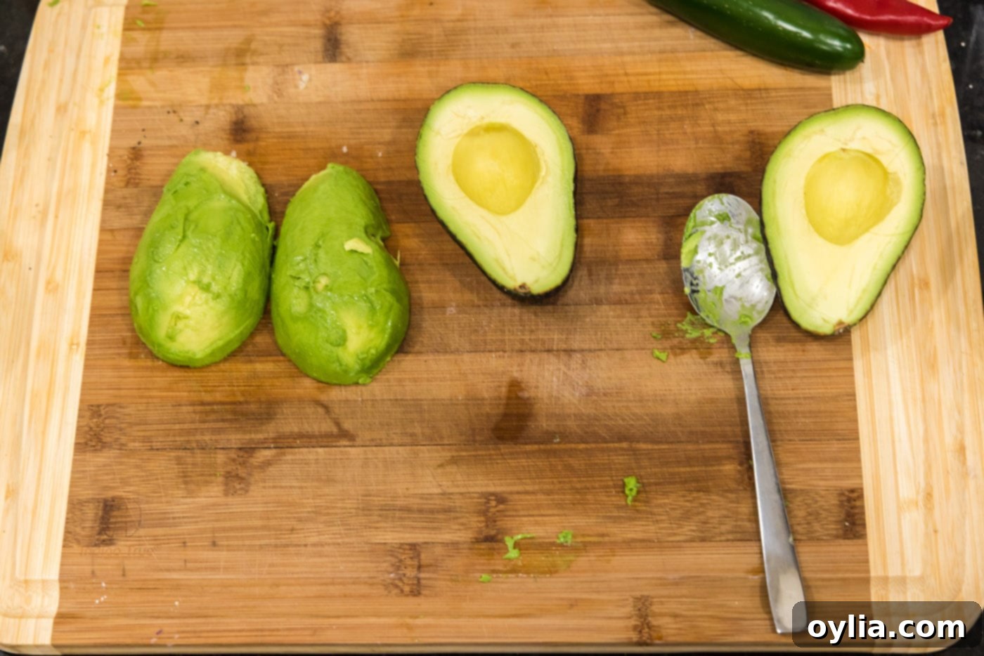 A spoon gently separating the avocado flesh from its skin on a cutting board