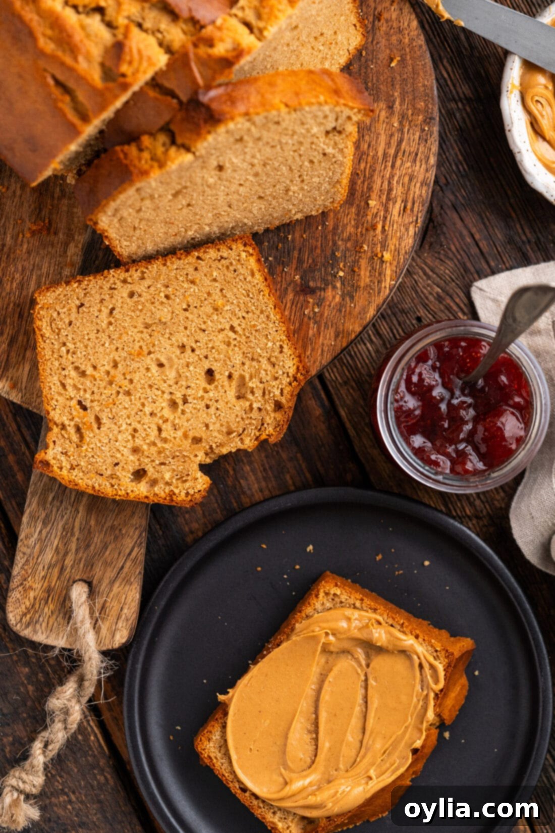 Slices of Homemade Peanut Butter Bread on a wooden board, with one slice generously topped with creamy peanut butter.
