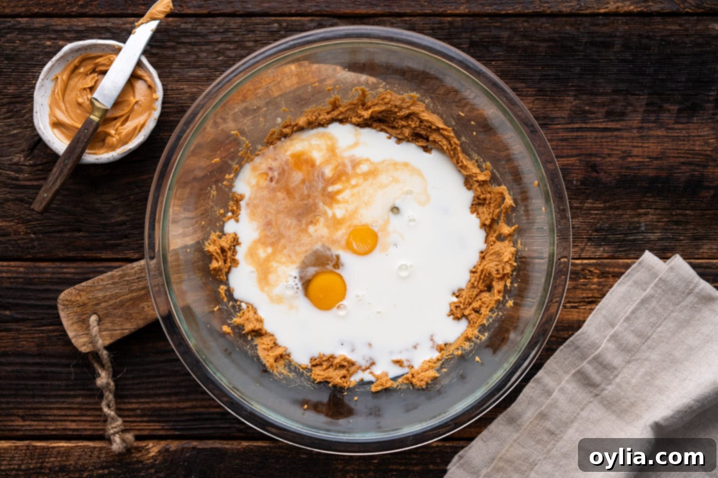 Wet ingredients including eggs, milk, and vanilla added to the peanut butter and sugar mixture in a bowl.