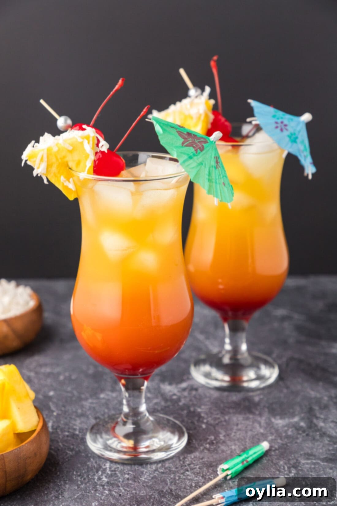 Two Malibu Sunset cocktails garnished with a pineapple wedge, cherry and umbrella