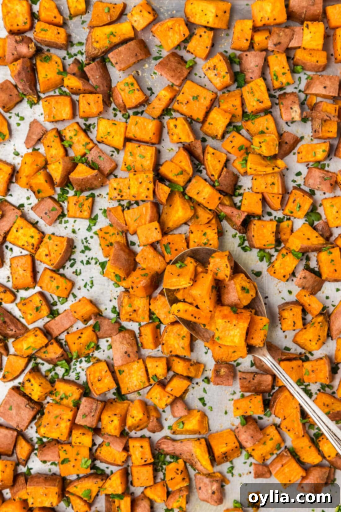 Sheet pan of golden-brown roasted sweet potatoes with a serving spoon, highlighting their crispy texture and delicious caramelization.