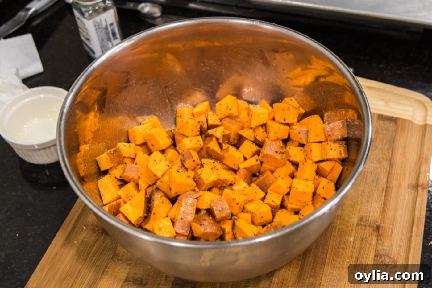 Cubed sweet potatoes being thoroughly tossed by hand with olive oil and a savory-sweet spice blend in a large mixing bowl.