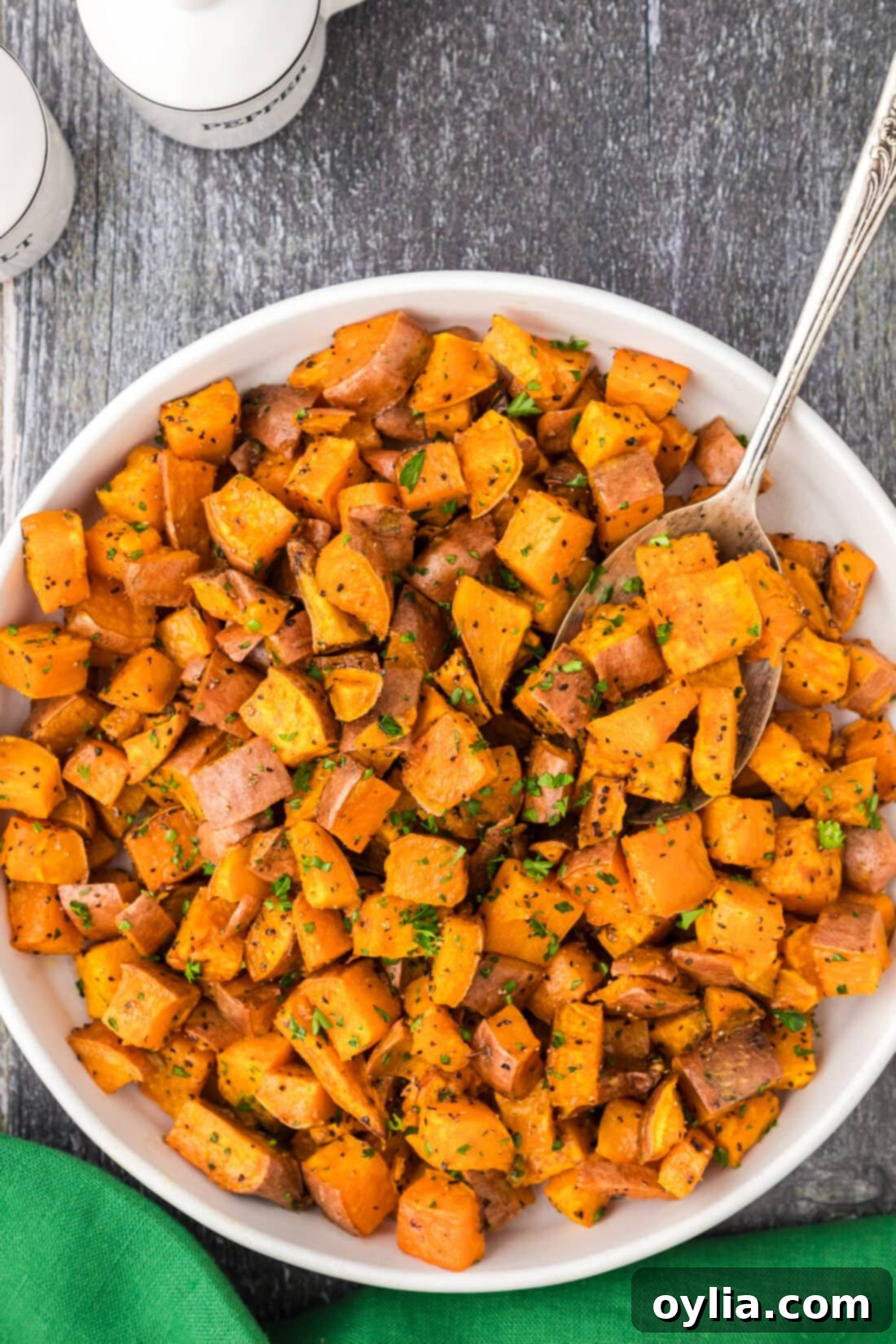 A bowl overflowing with glistening roasted sweet potatoes, perfect as a healthy and flavorful side dish, with a serving spoon.