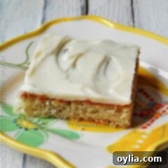 A close up photo of a banana bar with vanilla cream cheese frosting on a white plate.