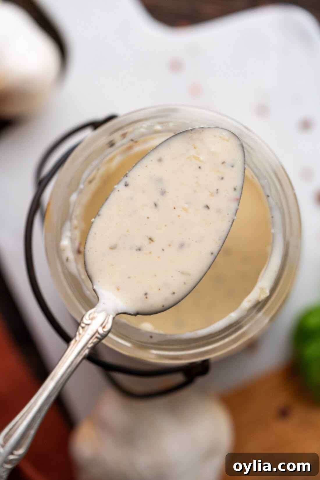 A spoon of Garlic Parmesan Wing Sauce being held above a jar, showing its creamy texture.