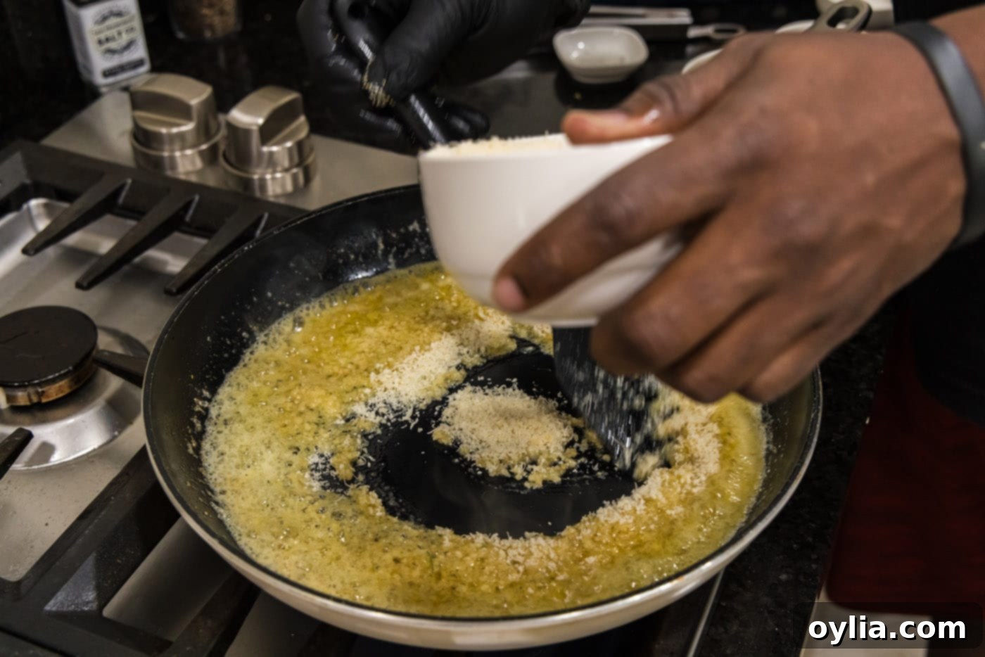 Gradually adding grated Parmesan cheese to the hot butter and garlic mixture, stirring constantly to create a smooth sauce.