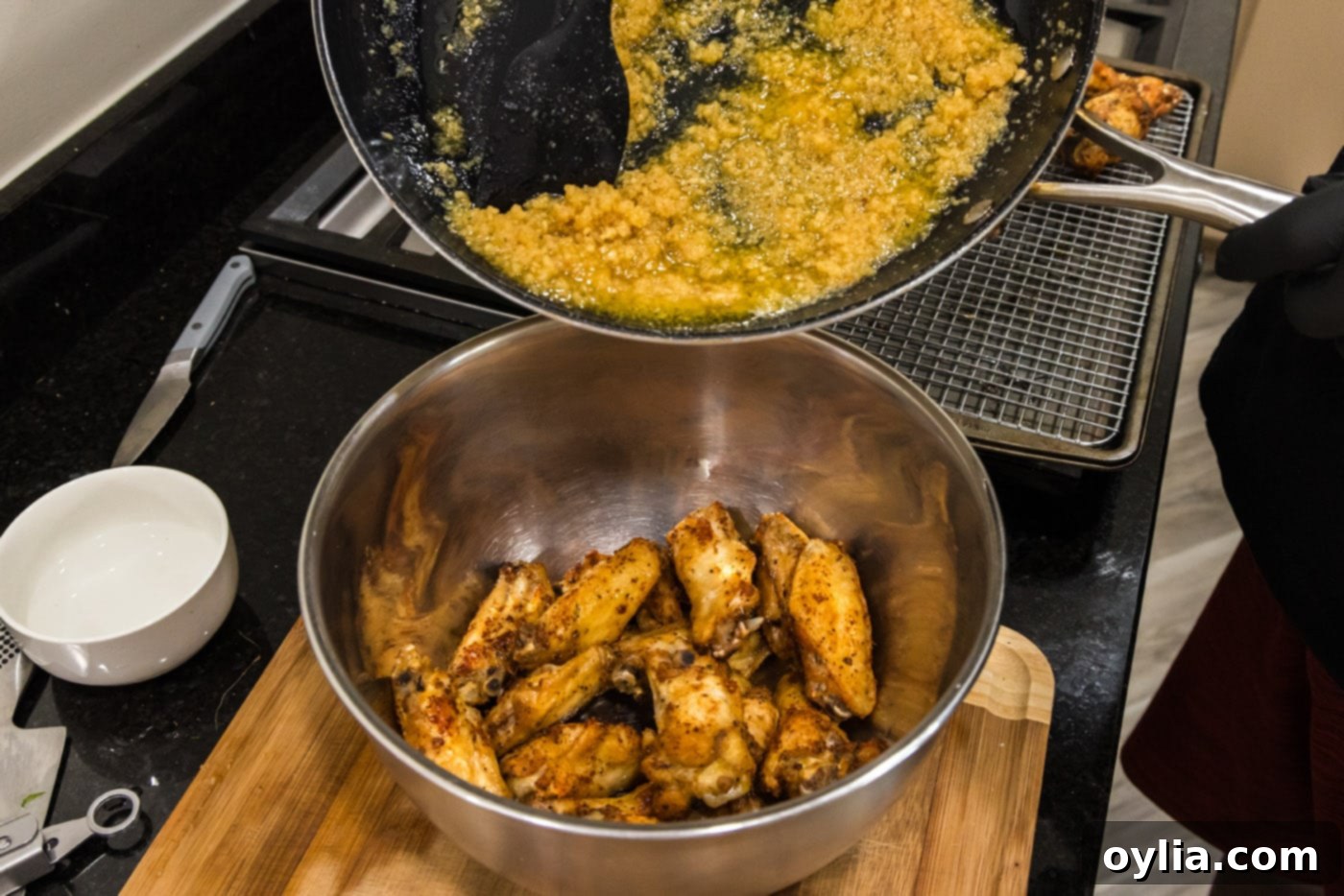 Pouring the creamy garlic parmesan sauce over a bowl of crispy fried chicken wings.