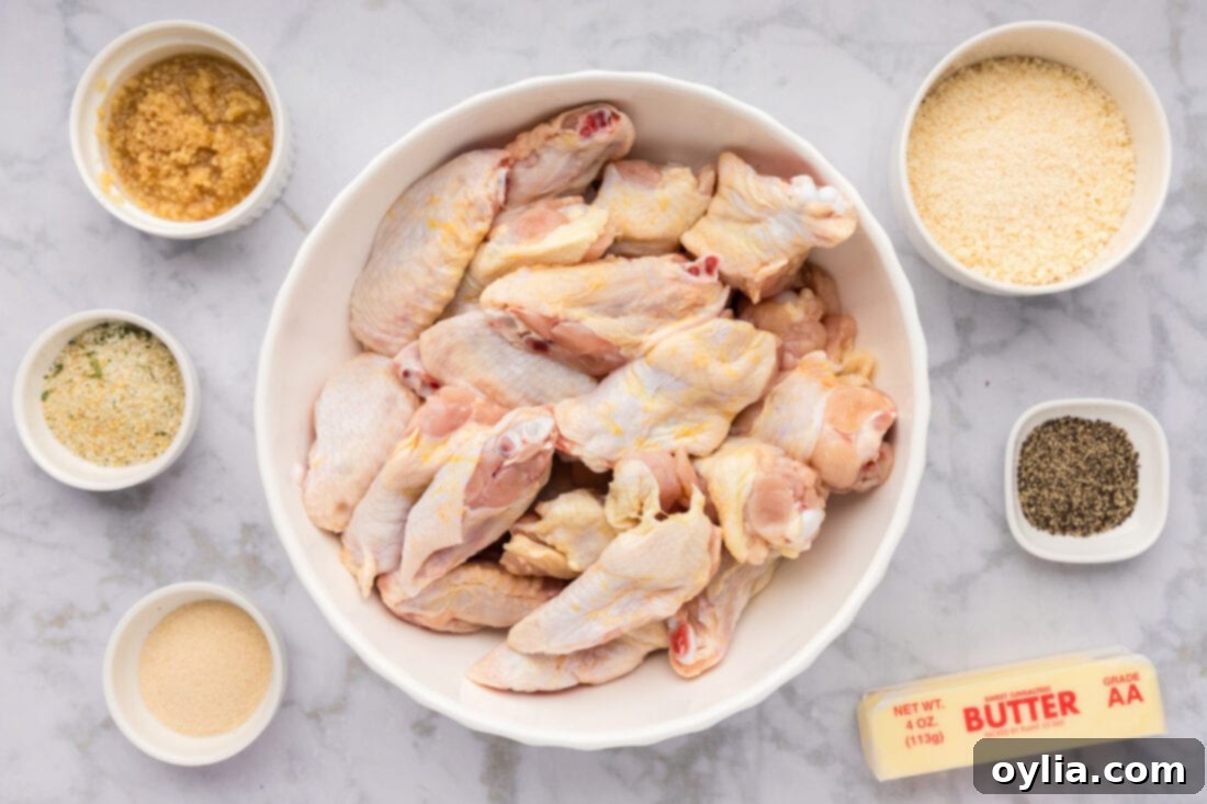 A collection of ingredients laid out on a table for making Garlic Parmesan Wings, including chicken wings, butter, minced garlic, parmesan cheese, and seasonings.