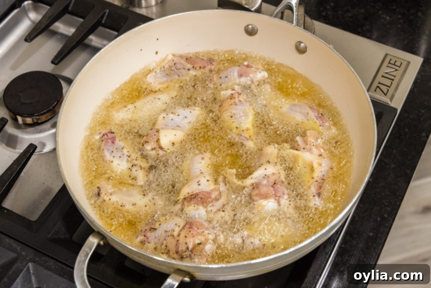 Chicken wings frying in hot oil in a deep skillet, achieving a golden color.