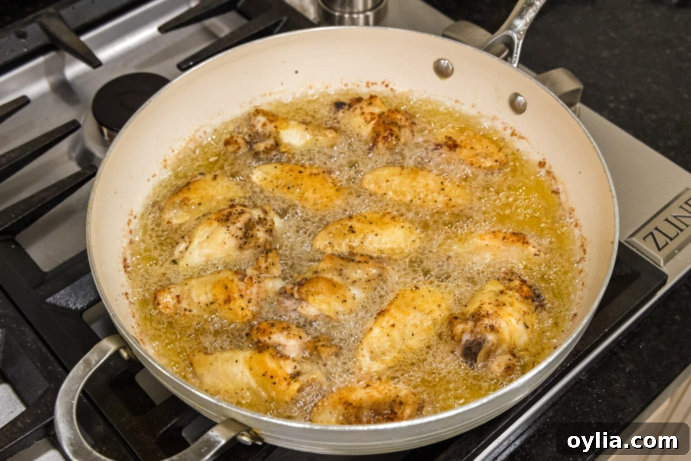 Several chicken wings frying in a skillet of oil, bubbling and browning.