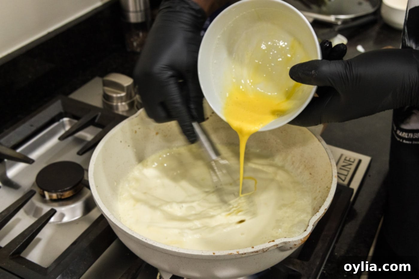 pouring whisked eggs into skillet of heavy cream while constantly whisking to combined
