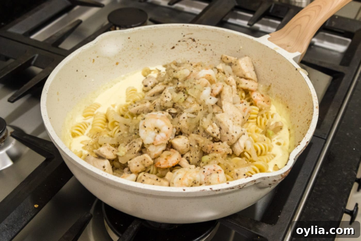adding chicken and shrimp mixture to skillet with pasta and carbonara sauce