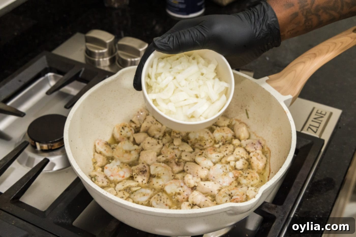 Hand adding chopped onion to skillet with chicken and shrimp mixture