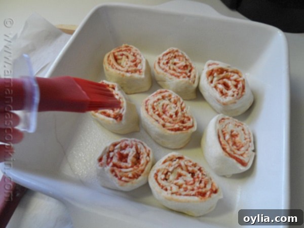 A tightly rolled log of pizza dough, filled with sauce and cheese, wrapped in parchment paper and prepared for chilling.
