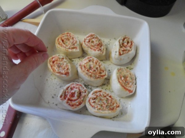 Perfectly sliced pizza roll ups arranged in a square baking pan, glistening with melted butter and sprinkled with seasonings.
