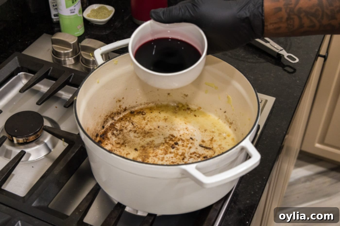 Pouring dry red wine into a Dutch oven to deglaze the pan after searing beef.