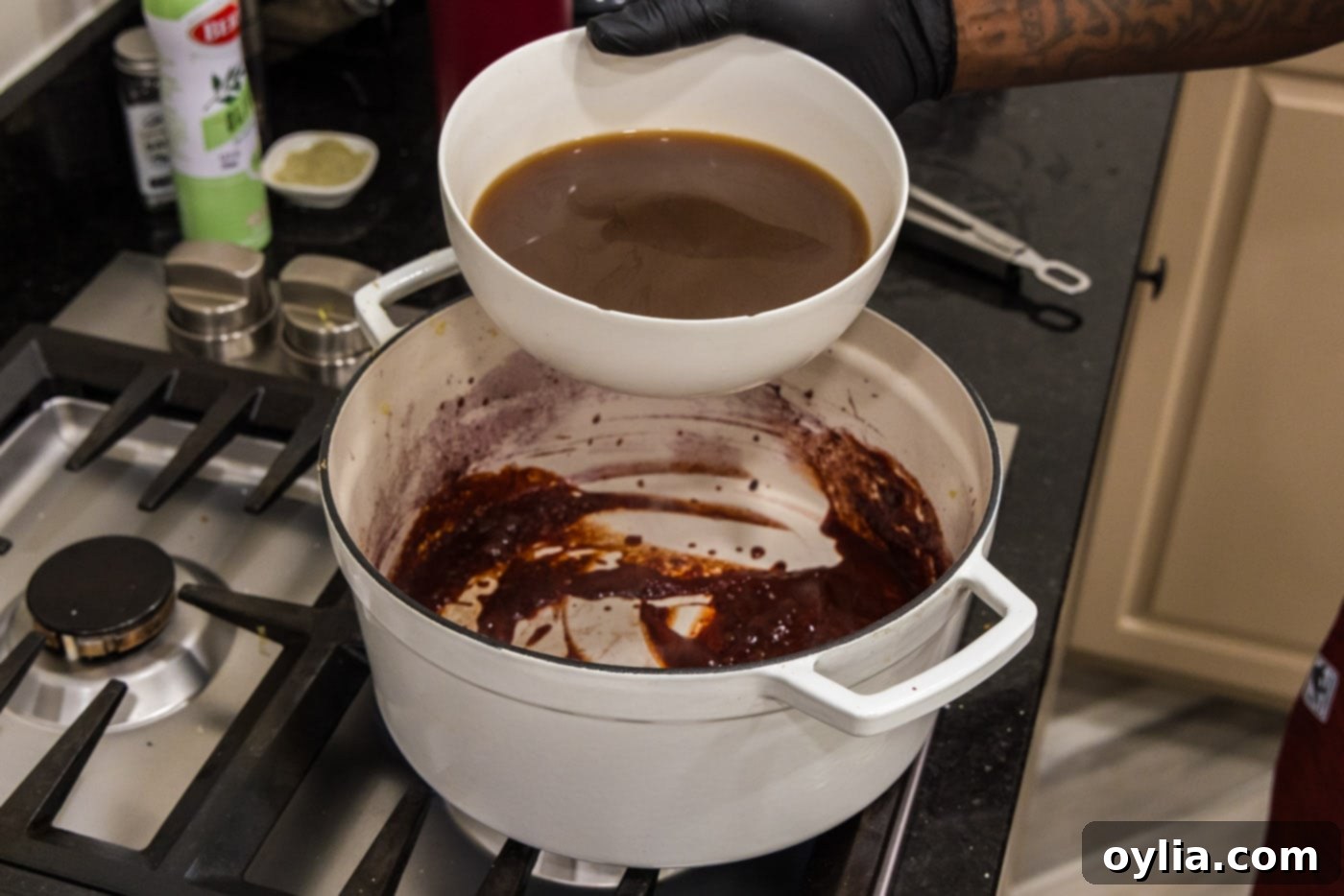 Adding beef broth to the red wine and tomato paste mixture in the Dutch oven, creating the braising liquid.