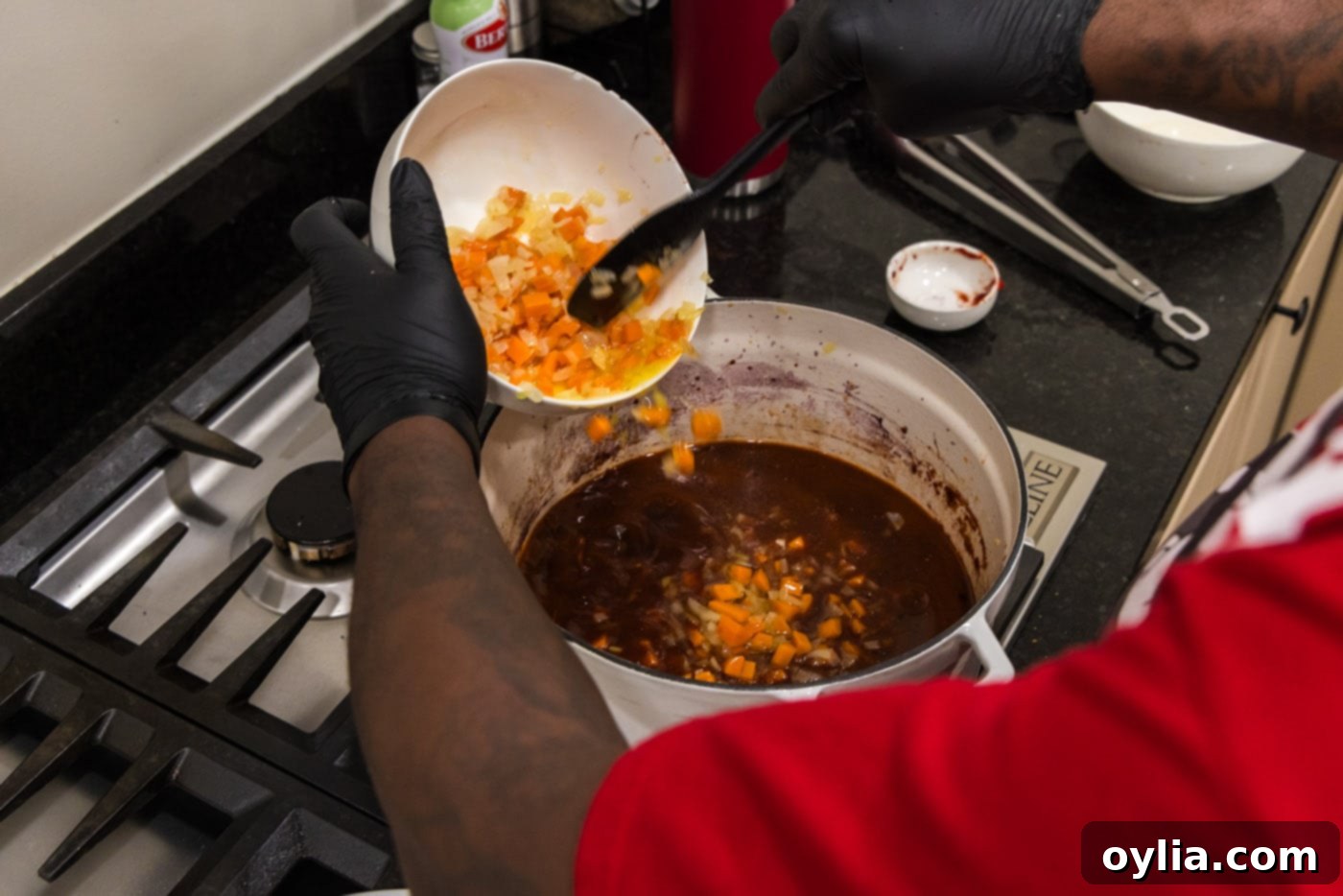 Adding sautéed carrots and onions back into the pot with the red wine sauce and beef broth.