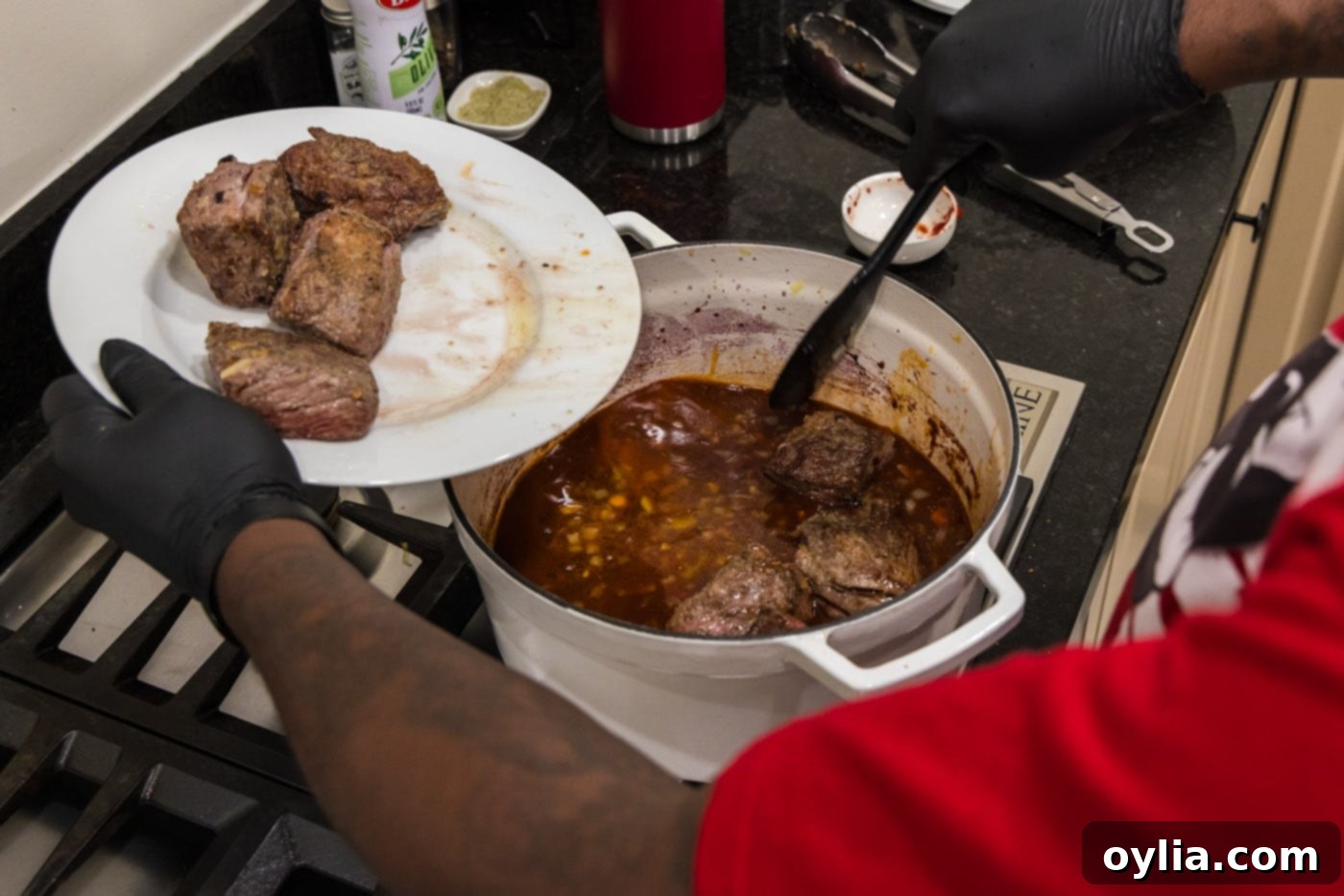 Placing seared short ribs into the Dutch oven with the rich red wine sauce and vegetables, preparing for braising.