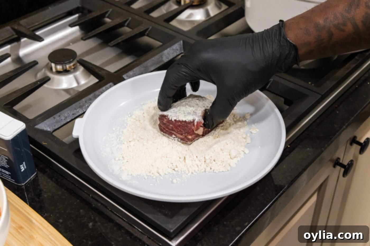 Dredging a seasoned beef short rib in all-purpose flour on a shallow plate.
