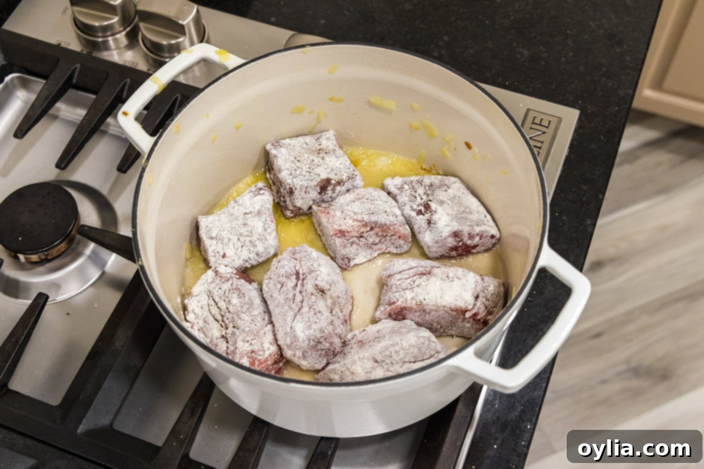 Flour-dredged beef short ribs searing to a golden brown in a Dutch oven on the stovetop.