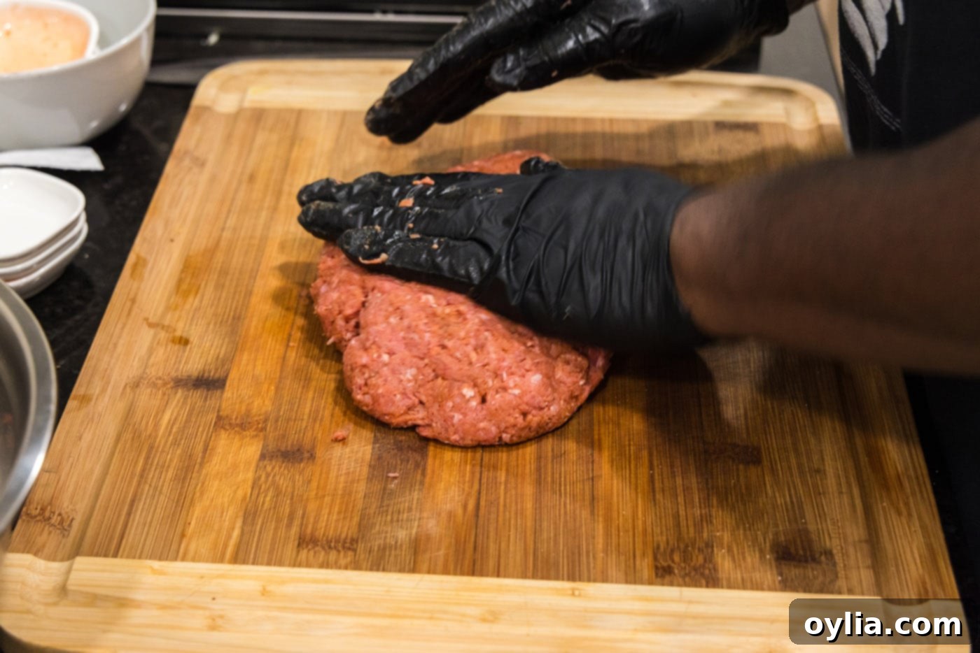 hands flattening burger meat on a cutting board