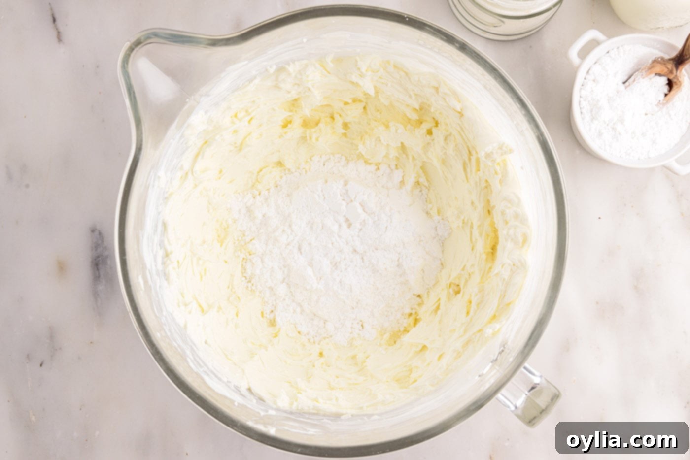 Powdered sugar being carefully added to the light and fluffy cream cheese mixture in a bowl, ready to be beaten until combined.