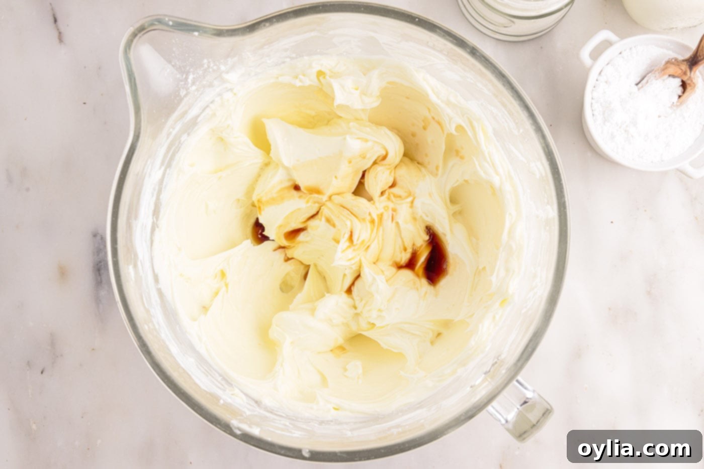 Vanilla extract being poured into the smooth cream cheese and powdered sugar mixture, adding an aromatic depth of flavor.
