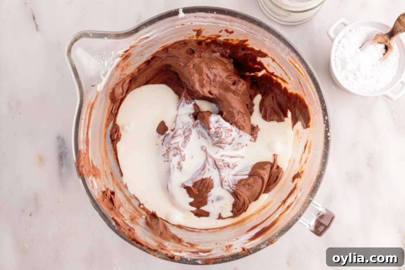 Heavy whipping cream being added to the chocolate cheesecake mixture in a large bowl, initiating the final whipping process to achieve fluffiness.