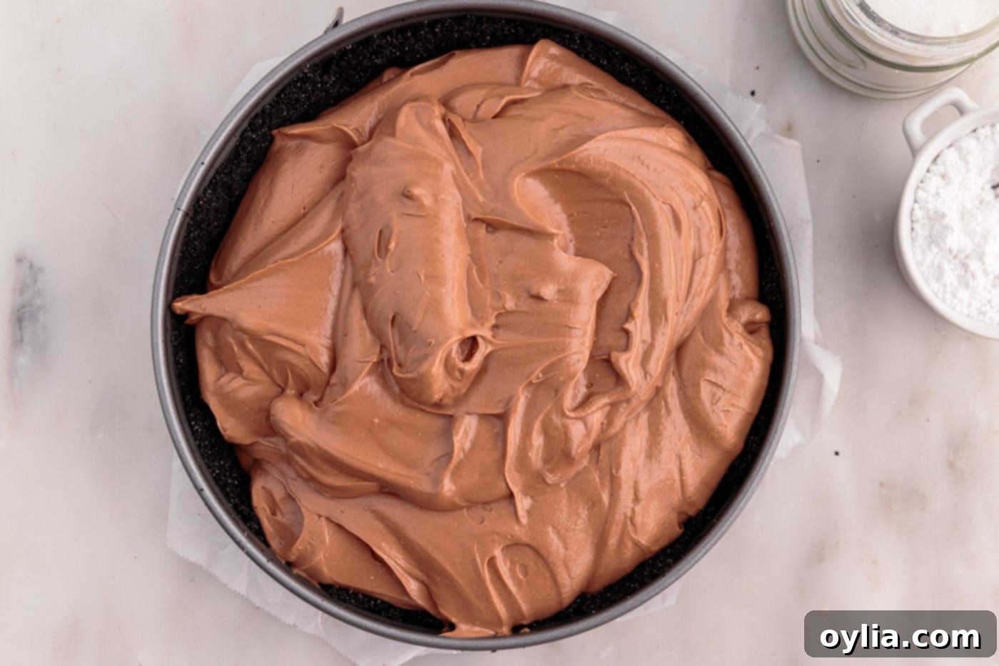 Smooth chocolate cheesecake mixture being meticulously spread evenly into the chilled chocolate graham cracker crust within a springform pan.