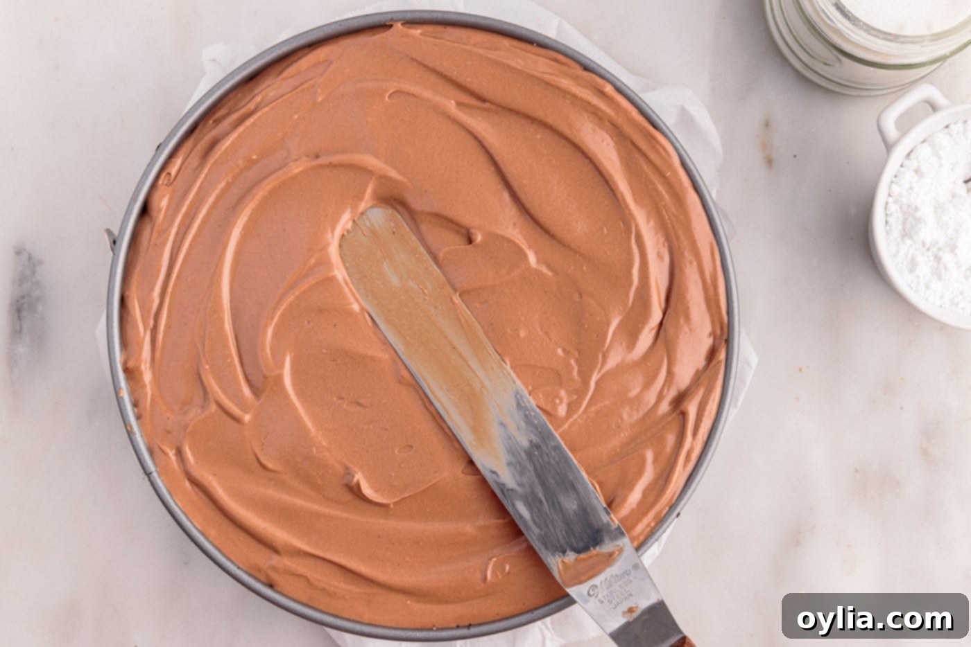 An offset spatula expertly smoothing the top surface of the no-bake chocolate cheesecake mixture in a springform pan, creating a perfectly flat and elegant finish.
