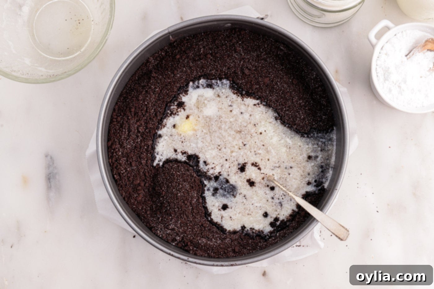 Melted butter being incorporated into the graham cracker crumbs and sugar, creating a sandy and cohesive mixture perfect for the cheesecake crust.