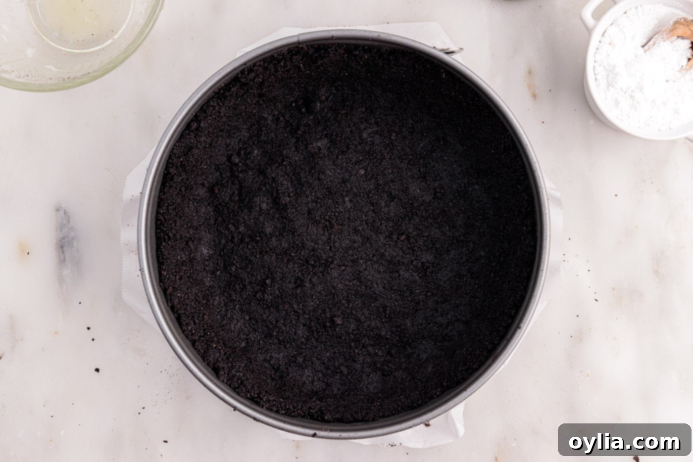 A perfectly formed and firmly pressed chocolate graham cracker crust chilling in a springform pan, showing its readiness to hold the creamy filling.