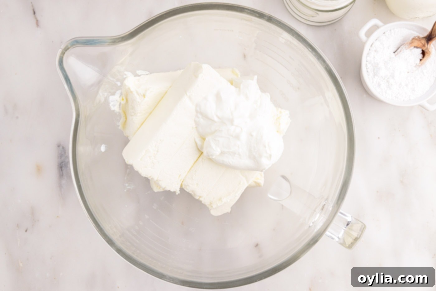 Softened cream cheese and sour cream being beaten together in a large mixing bowl, creating a smooth and airy base for the cheesecake filling.