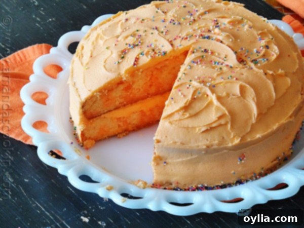 Full orange poke cake with slices cut out, ready to serve, adorned with bright orange frosting.