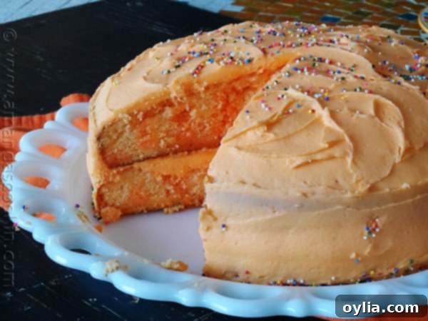 Side view of the completed orange poke cake, revealing its moist layers infused with gelatin, and topped with rich orange buttercream.