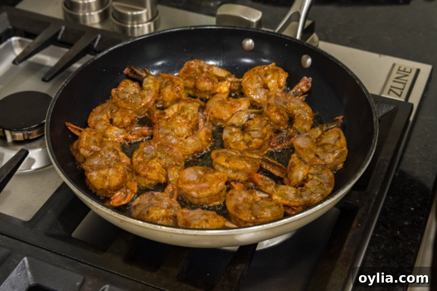 Seasoned shrimp sizzling in a hot skillet, beginning to cook